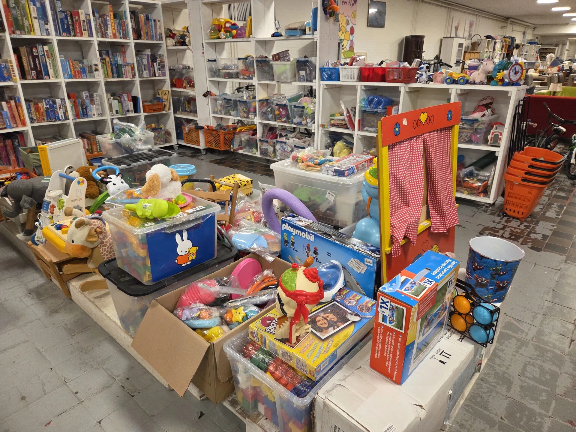 Uitgestalde speelgoed en kinderspullen in een kringloopwinkel, inclusief bouwsets, poppen en diverse artikelen op tafels en s