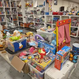 Uitgestalde speelgoed en kinderspullen in een kringloopwinkel, inclusief bouwsets, poppen en diverse artikelen op tafels en s