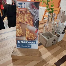 Menukaart 'La Poubelle 't Koffihuukske' met afbeelding van gebak, op tafel in de winkel
