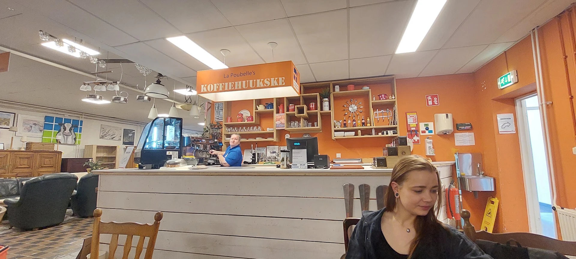 Koffiebalie 'Koffiehuiskje' met oranje stellingkast en bediening achter de balie