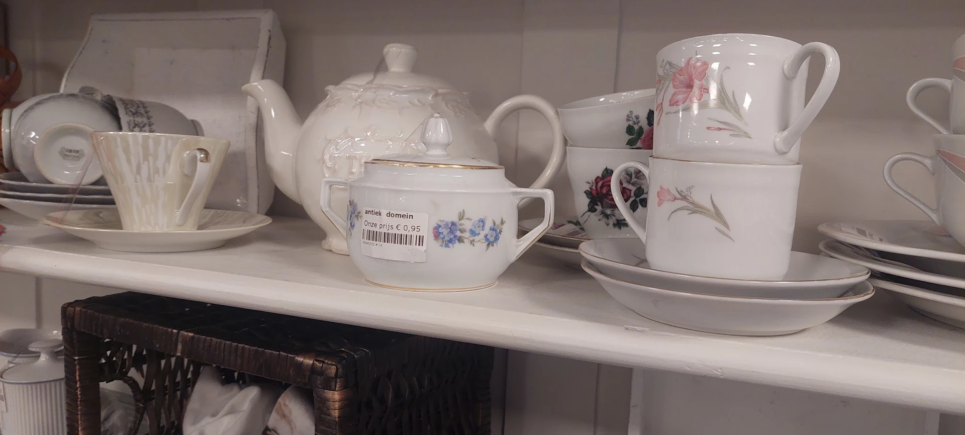 Wit serviesgoed met bloemmotieven op een winkelplank, waaronder een theepot, kopjes en schotels