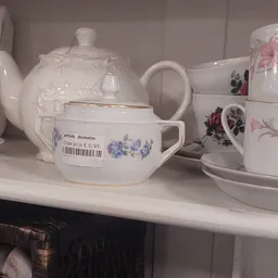 Wit serviesgoed met bloemmotieven op een winkelplank, waaronder een theepot, kopjes en schotels