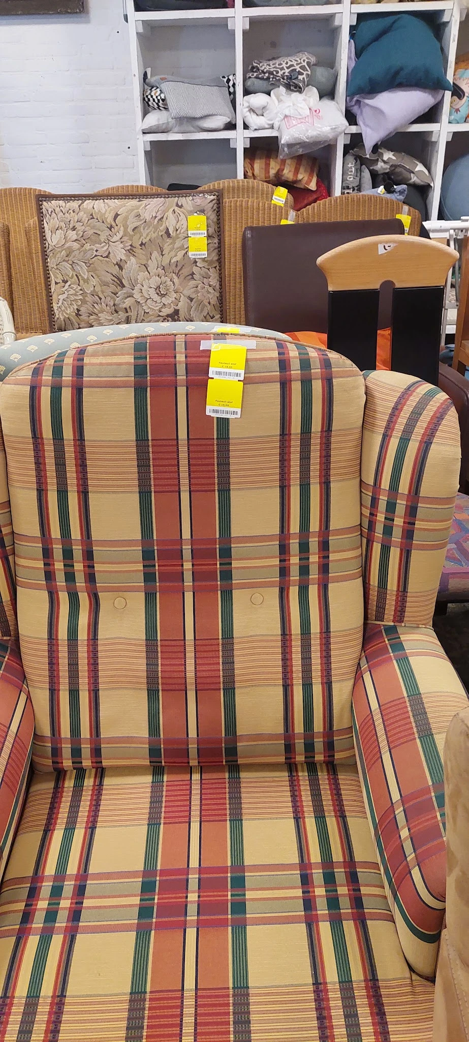 Close-up van een gestreepte fauteuil met rood-groen-gele ruitpatroon en geel verkoopkaartje