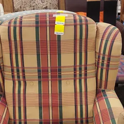 Close-up van een gestreepte fauteuil met rood-groen-gele ruitpatroon en geel verkoopkaartje