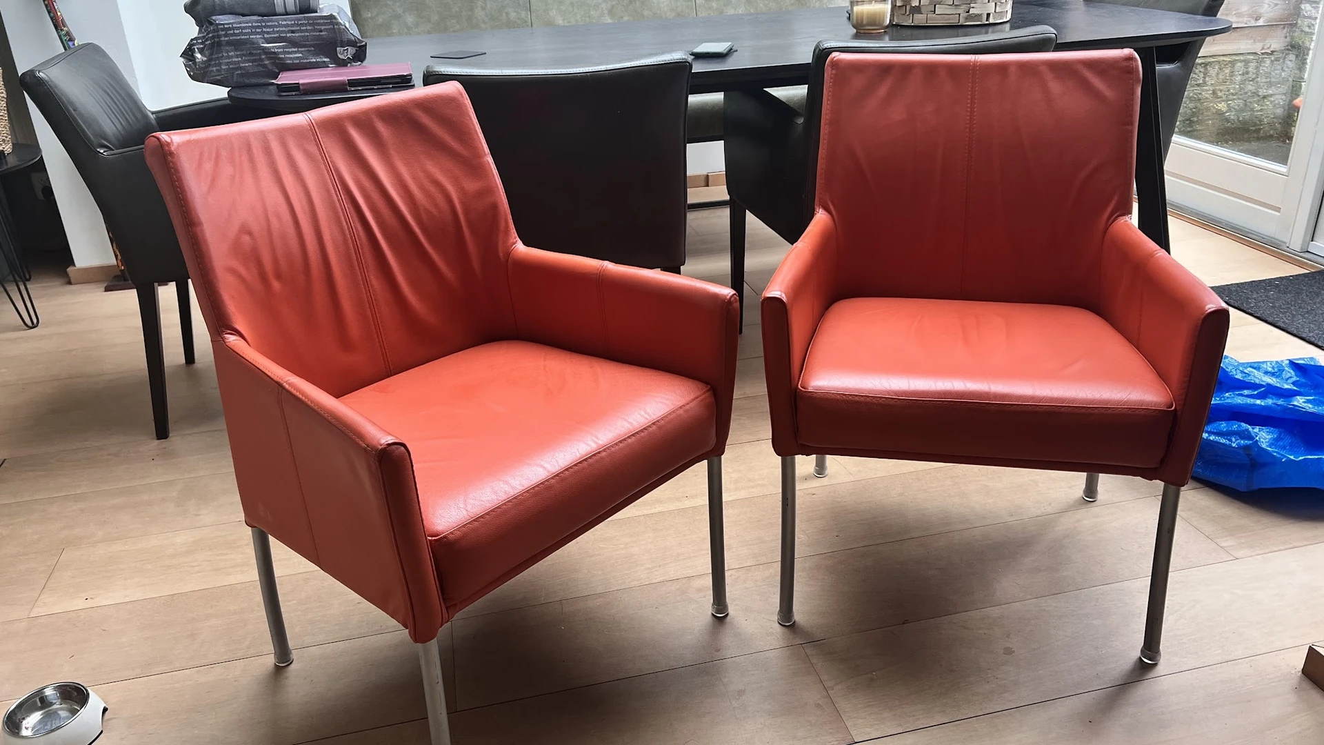 Twee rode/koraalkleurige fauteuils met armleuningen en metalen poten naast elkaar op een betonnen vloer