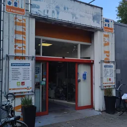 Gevel van kringloopwinkel La Poubelle met rode deuren, openingstijdenstickers en informatieborden