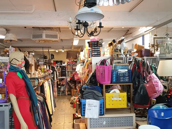 Winkelvloer van kringloopwinkel met rekken vol kleding, diverse items in dozen en manden, goed verlicht