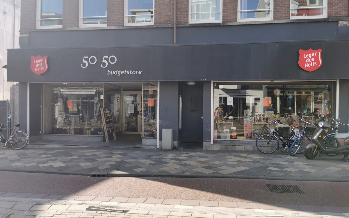 Gevel van Leger des Heils 50|50 Budgetstore aan Middenweg in Amsterdam met donkergrijze pui, winkelnaam zichtbaar, etalagerui