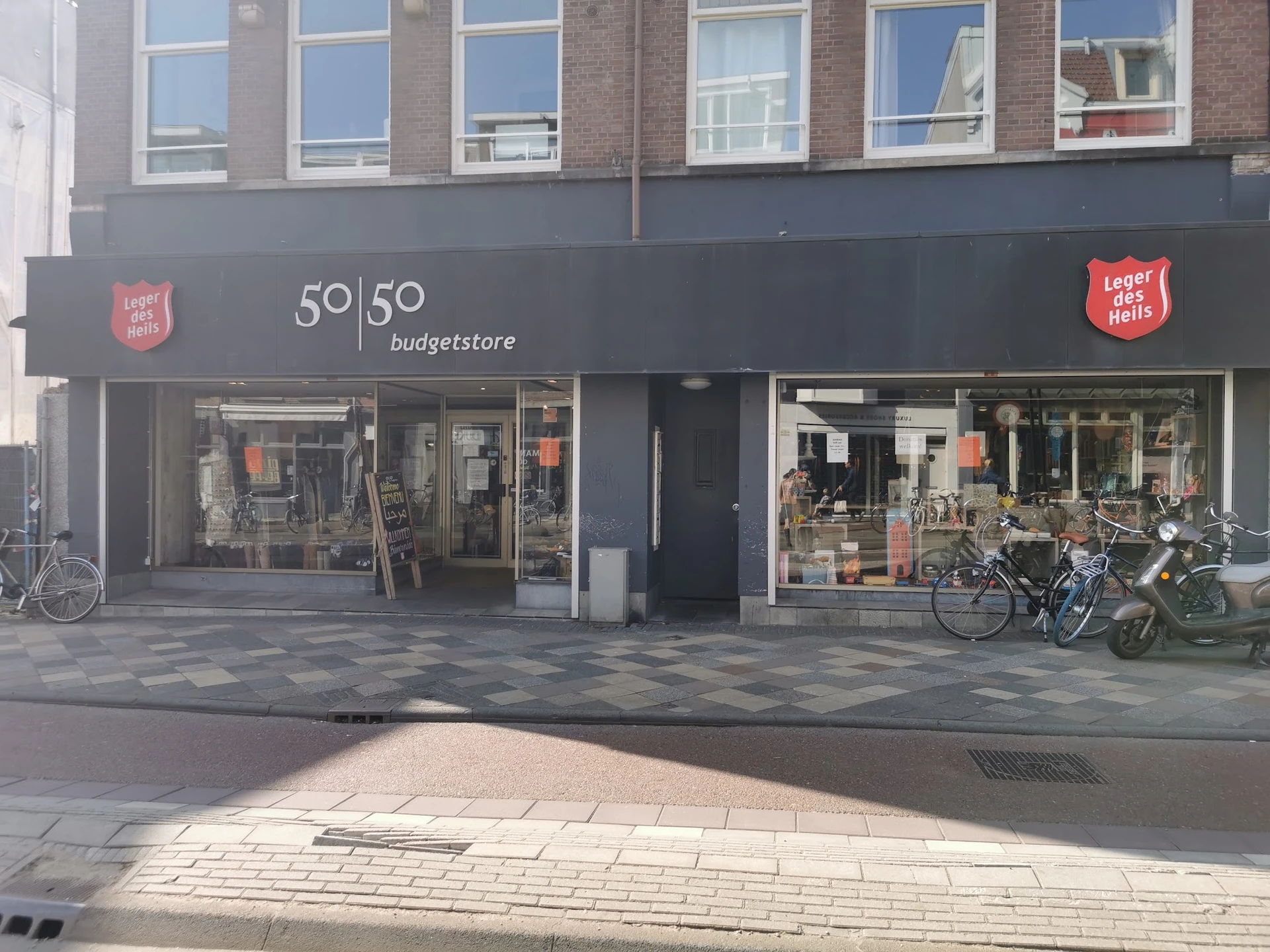 Gevel van Leger des Heils 50|50 Budgetstore aan Middenweg in Amsterdam met donkergrijze pui, winkelnaam zichtbaar, etalagerui
