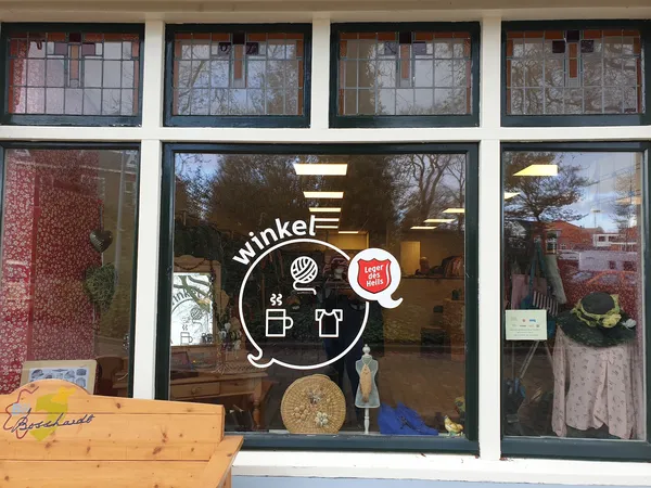 Winkelruit van kringloopwinkel met wit logo en uitgestalde spullen in etalage