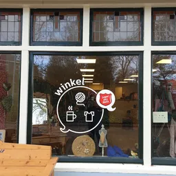 Winkelruit van kringloopwinkel met wit logo en uitgestalde spullen in etalage