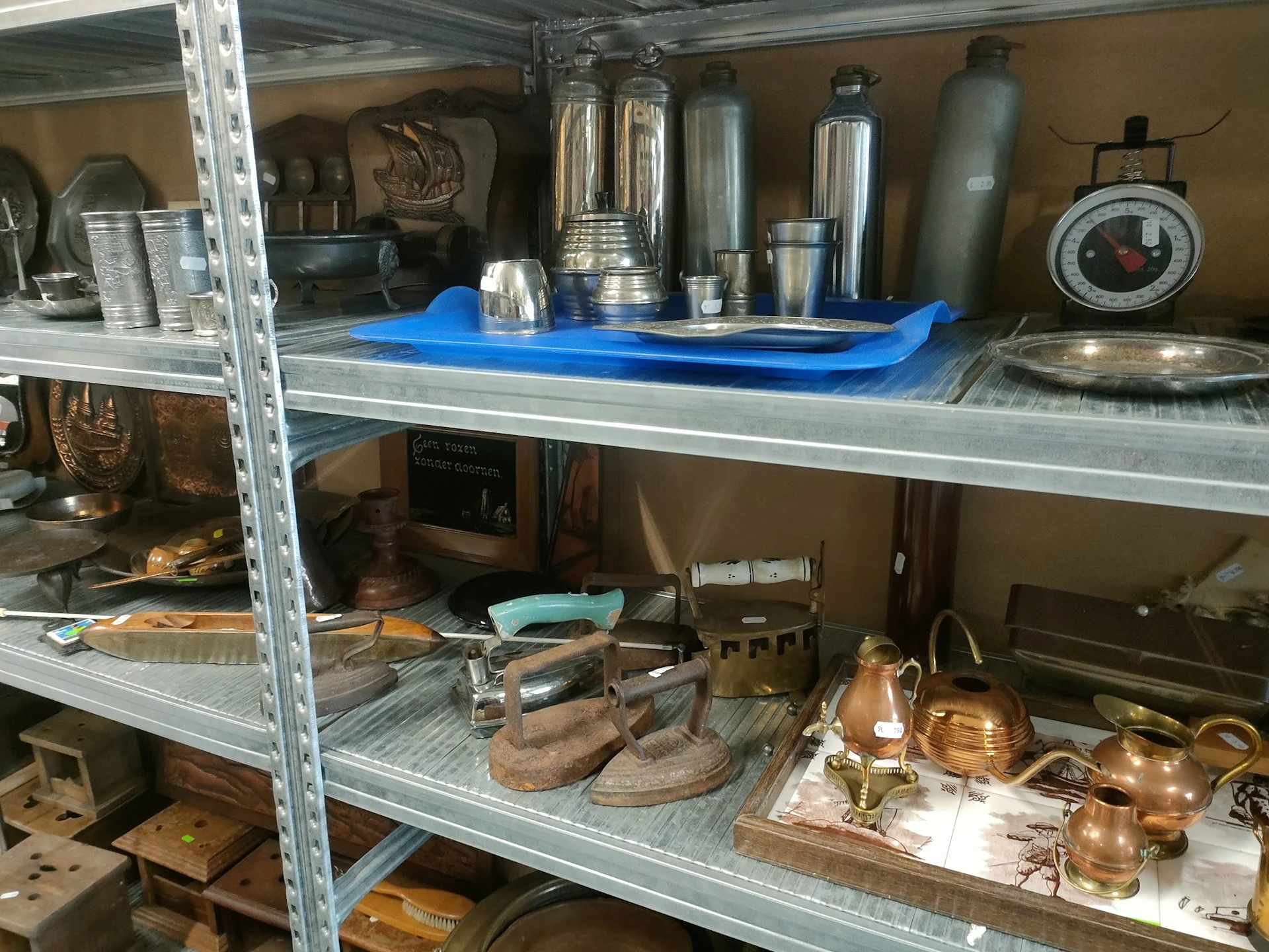 Metalen stellingkasten met huishoudelijke artikelen: thermoskannen, koppelingen, koperwerk en keukenspullen