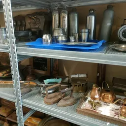 Metalen stellingkasten met huishoudelijke artikelen: thermoskannen, koppelingen, koperwerk en keukenspullen