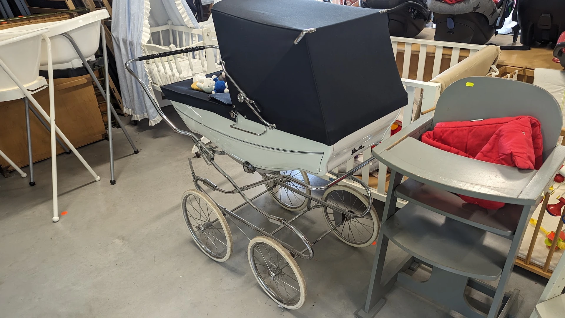 Vintage kinderwagen met zwart luifel op wielen in een magazijn.