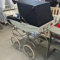 Vintage kinderwagen met zwart luifel op wielen in een magazijn.