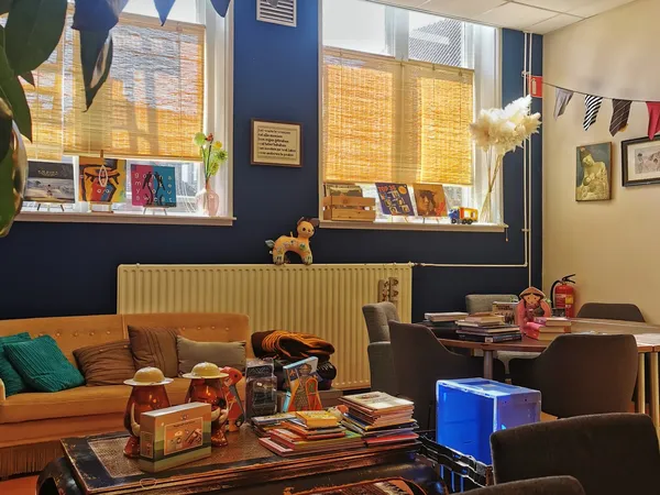 Woonkamerhoek met oranje bank, bruine fauteuils en tafels met tweedehands spullen, boeken en decoratie