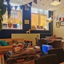 Woonkamerhoek met oranje bank, bruine fauteuils en tafels met tweedehands spullen, boeken en decoratie