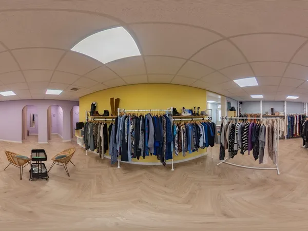 Ruim winkelbinnenland met gele kledingrek en rekken met tweedehands kleding, houten vloer en moderne plafondverlichting