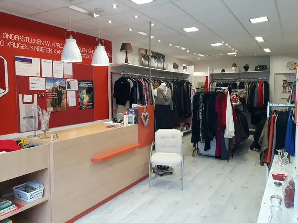 Winkelvloer met kledingrekken, balie en rode muur in kringloopwinkel