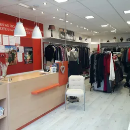 Winkelvloer met kledingrekken, balie en rode muur in kringloopwinkel