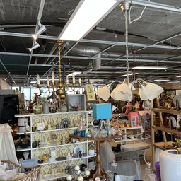 Overzicht van kringloopwinkelinterieur met stellingen, lampen, serviesgoed en diverse huishoudelijke artikelen