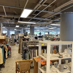 Ruime winkelhal met stellingen vol kleding, huishoudartikelen en meubels, pilaren, goed verlicht