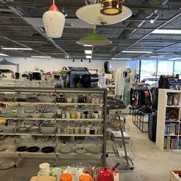 Winkelvloer met stellingen vol huishoudspullen, kleding en boeken, verlicht door hangende lampen