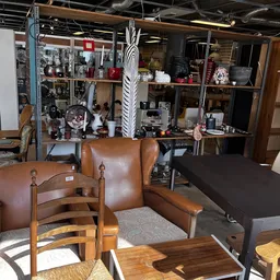 Interieur met bruine lederen fauteuil, houten stoel en zwarte tafel voor een stellage vol huishoudartikelen en decoraties