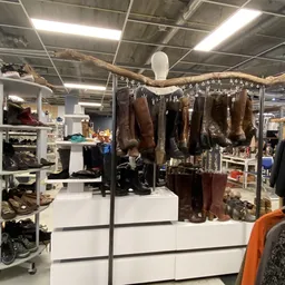 Uitgestalde laarzen en schoenen aan hangers en op stellingen in een kringloopwinkel