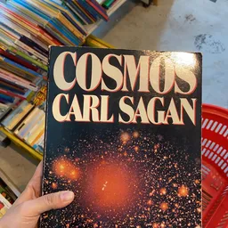 Boek 'Cosmos' van Carl Sagan met sterrenhemel op de omslag, gehouden in een hand