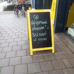 Geel bord met zwart krijtbord en handgeschreven Nederlandse tekst en telefoonnummer