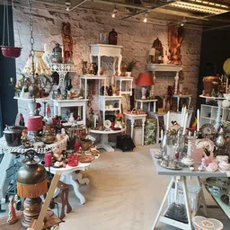 Interieur van kringloopwinkel met veel vintage en decoratieve spullen op witte stellingen tegen bakstenen muur
