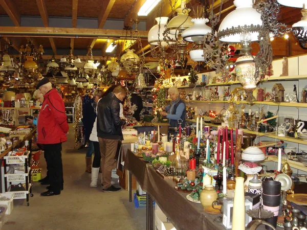 Winkelinterieur met houten balken, verlichte schappen vol decoratieve items, kaarsen en kerstversiering, enkele bezoekers lop