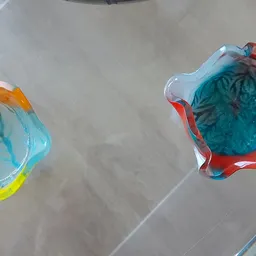 Twee gekleurde glazen decoratieve voorwerpen met blauw, rood, geel en oranje tinten op een witte oppervlak