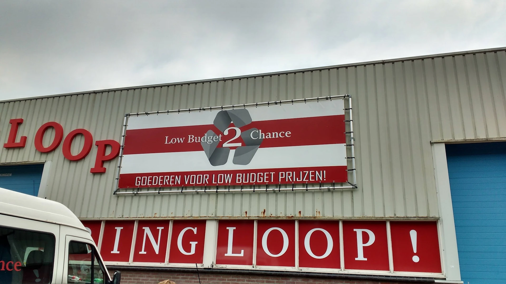 Gevel van kringloopwinkel Low Budget 2 Chance met rode en witte borden en tekstbanden