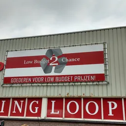 Gevel van kringloopwinkel Low Budget 2 Chance met rode en witte borden en tekstbanden