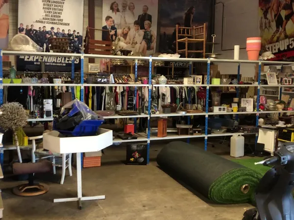 Winkelvloer met blauwe stellingen vol kleding, boeken en huishoudspullen, kunstgras en diverse meubelstukken