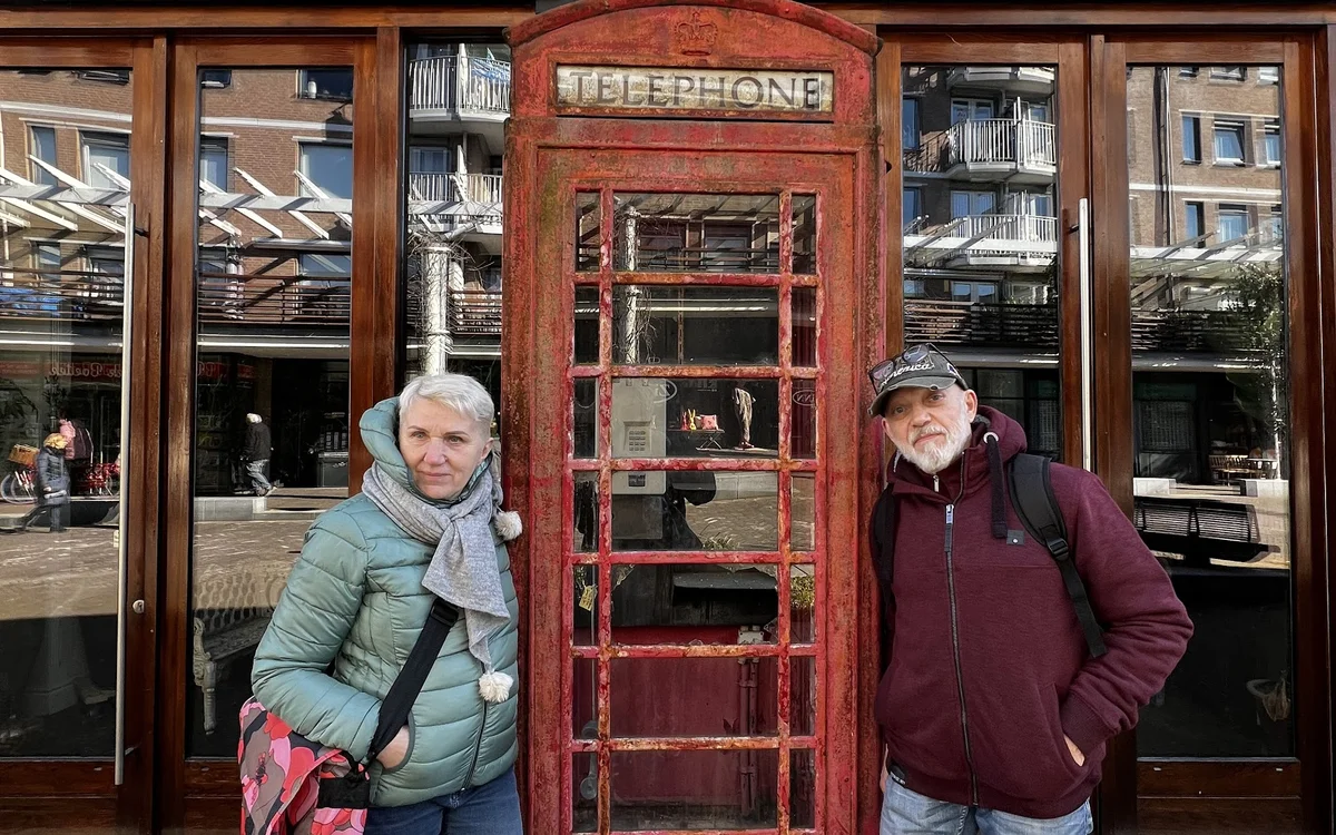 Twee personen poseren voor een rode telefooncell voor de winkelruit van Lycka Secondhand