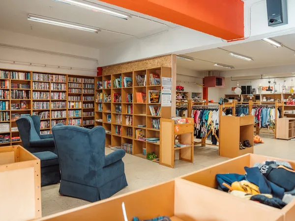 Winkelvloer met boekenkasten, kledingrekken, blauwe stoelen en houten schappen met tweedehands artikelen