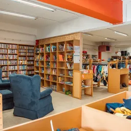 Winkelvloer met boekenkasten, kledingrekken, blauwe stoelen en houten schappen met tweedehands artikelen