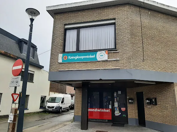 Voorgevel van kringloopwinkel met bakstenen gevel, blauw en rood winkellogo, etalagevenster en ingang met markies