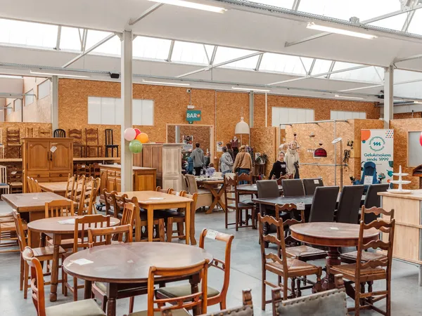 Winkelvloer met diverse houten meubels, tafels en stoelen uitgestald in een ruime hal met glazen dak