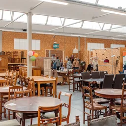Winkelvloer met diverse houten meubels, tafels en stoelen uitgestald in een ruime hal met glazen dak