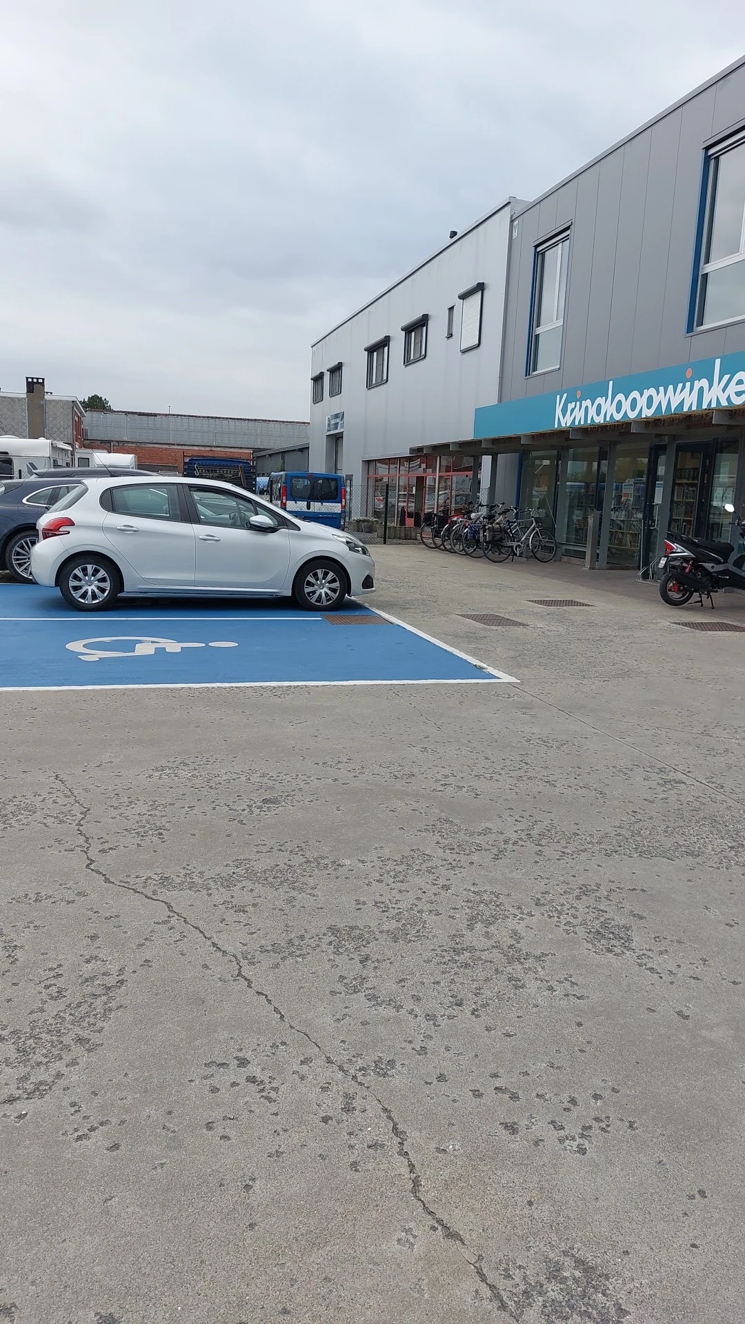 Witte auto geparkeerd op elektrisch voertuig laadplek voor een kringloopwinkel met winkelpui op achtergrond