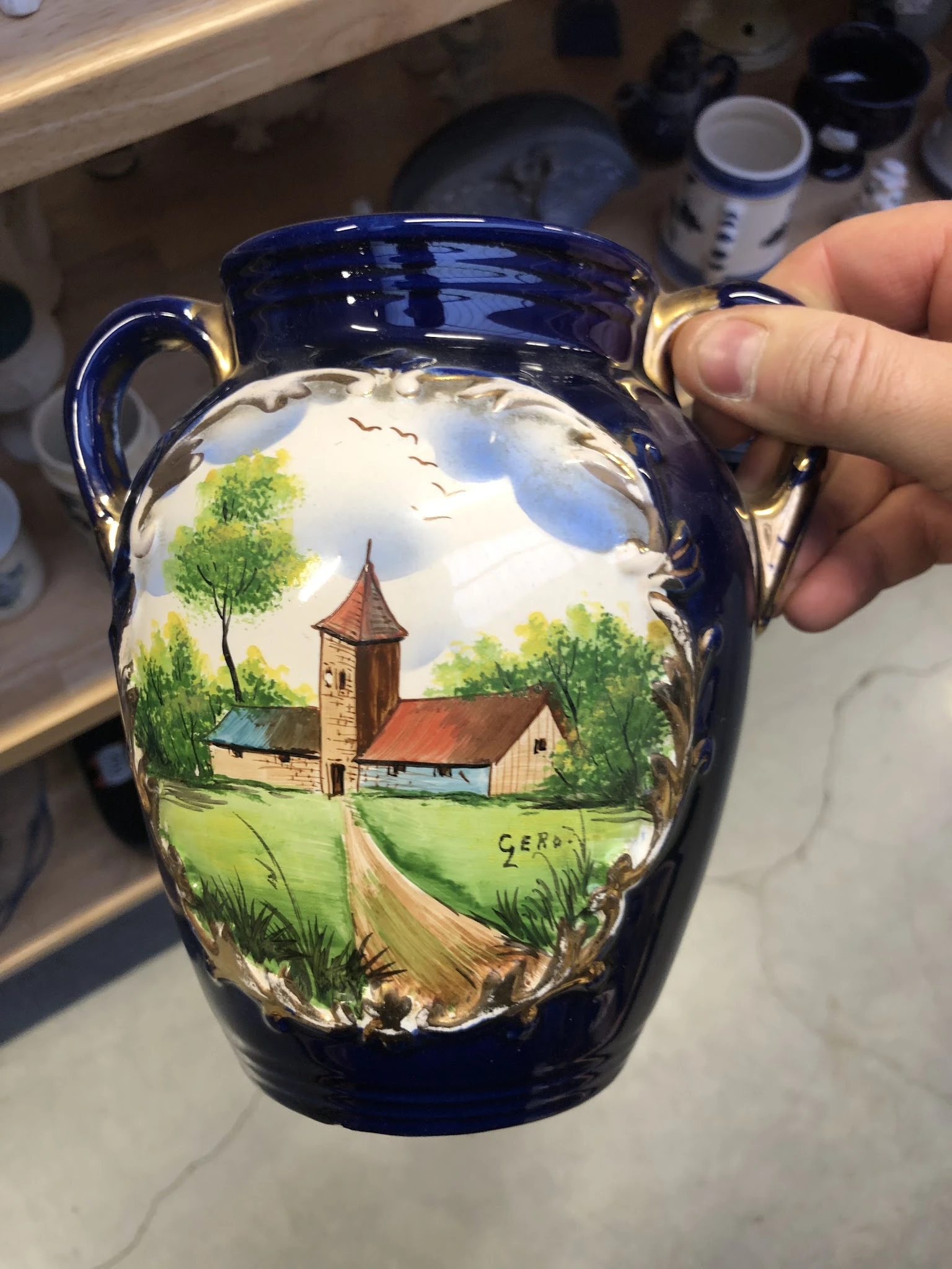 Blauwe aardewerk kan met handgeschilderd landschapsmotief van een kerk tussen groene bomen