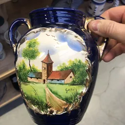 Blauwe aardewerk kan met handgeschilderd landschapsmotief van een kerk tussen groene bomen