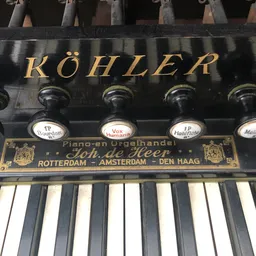 Close-up van een Köhler piano-orgel met toetsen en registerknopen met labels