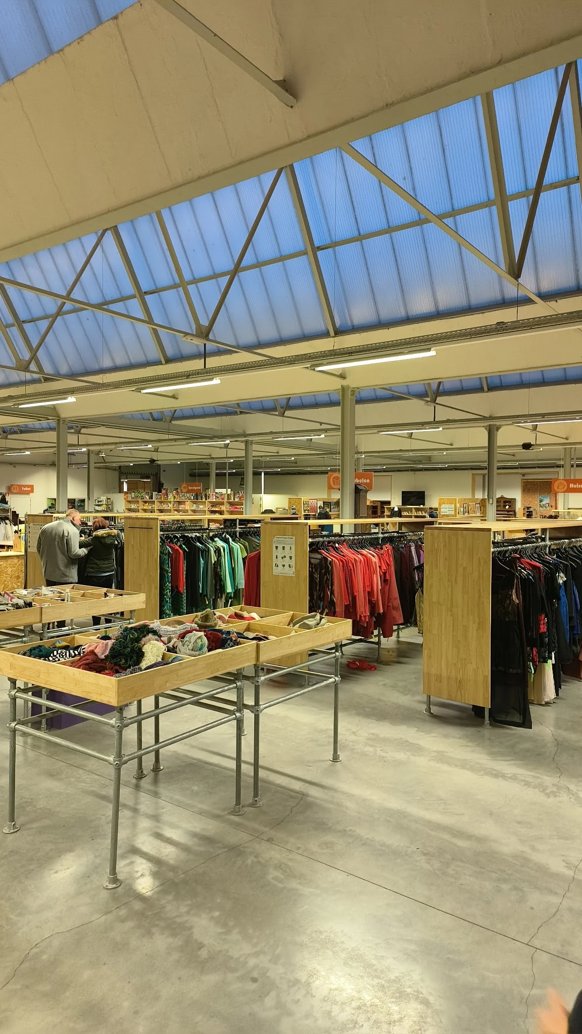 Ruim winkelinterieur met houten stellingen vol tweedehands kleding en een centrale tafel met artikelen