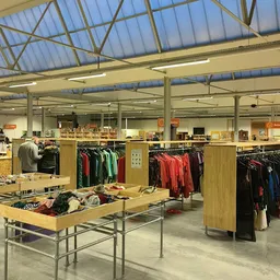 Ruim winkelinterieur met houten stellingen vol tweedehands kleding en een centrale tafel met artikelen