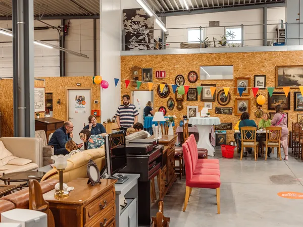 Winkelvloer met vintage meubels, decoraties aan kurken wand, bezoekers die rondkijken en winkelen